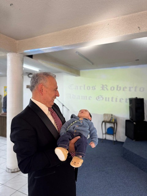 Pastor sosteniendo al bebé Carlos Roberto